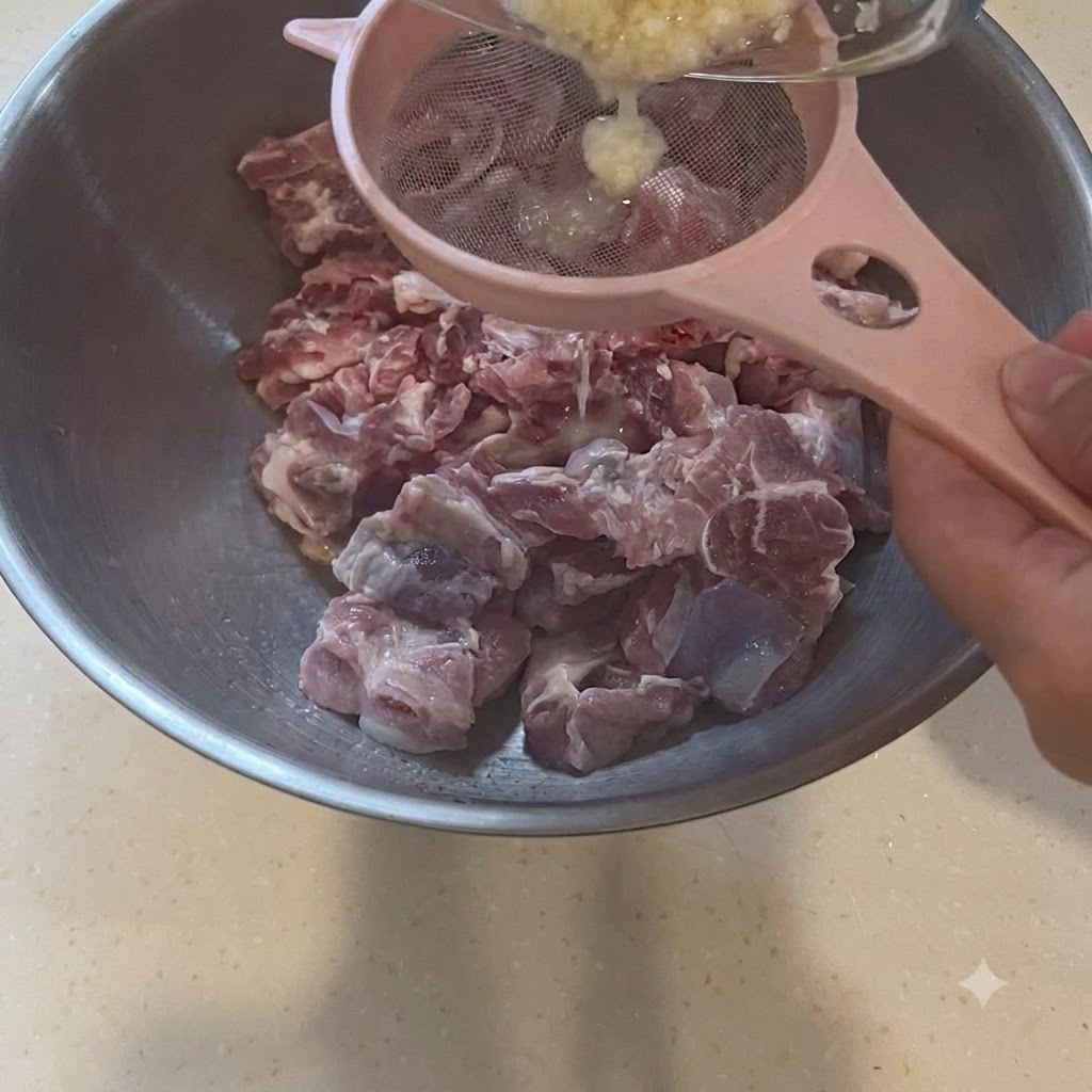 Pasta czosnkowa przecedzana przez różowe sitko bezpośrednio do miski z surowym mięsem.