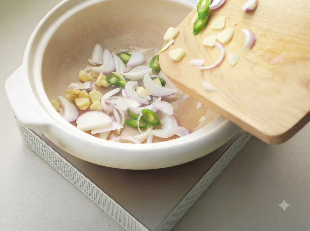Pokrojona cebula, czosnek i chili skwierczące w białym ceramicznym garnku.