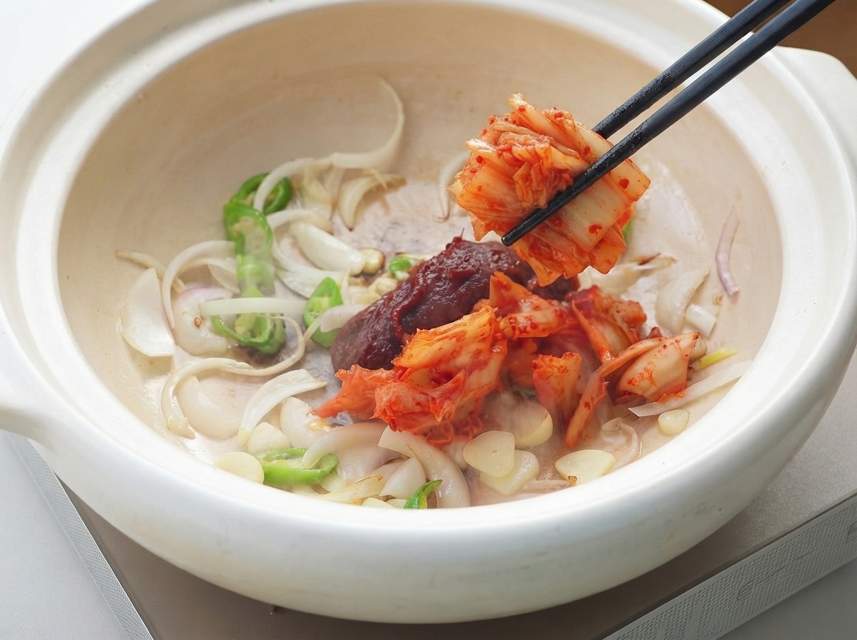 Koreańska pasta chili i kimchi dodawane do garnka z warzywami aromatycznymi za pomocą pałeczek.
