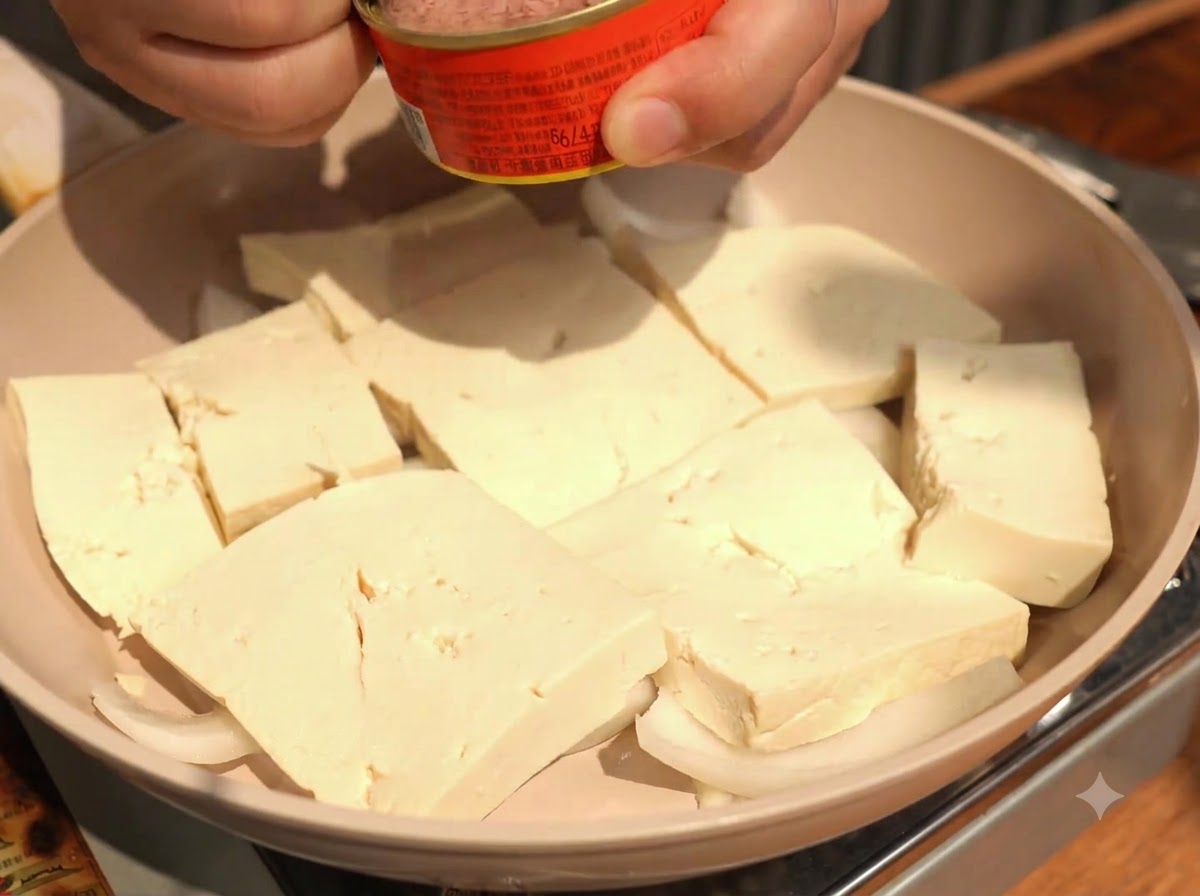 Nakładanie łyżką kawałków tuńczyka z puszki bezpośrednio na środek ułożonych plastrów tofu.