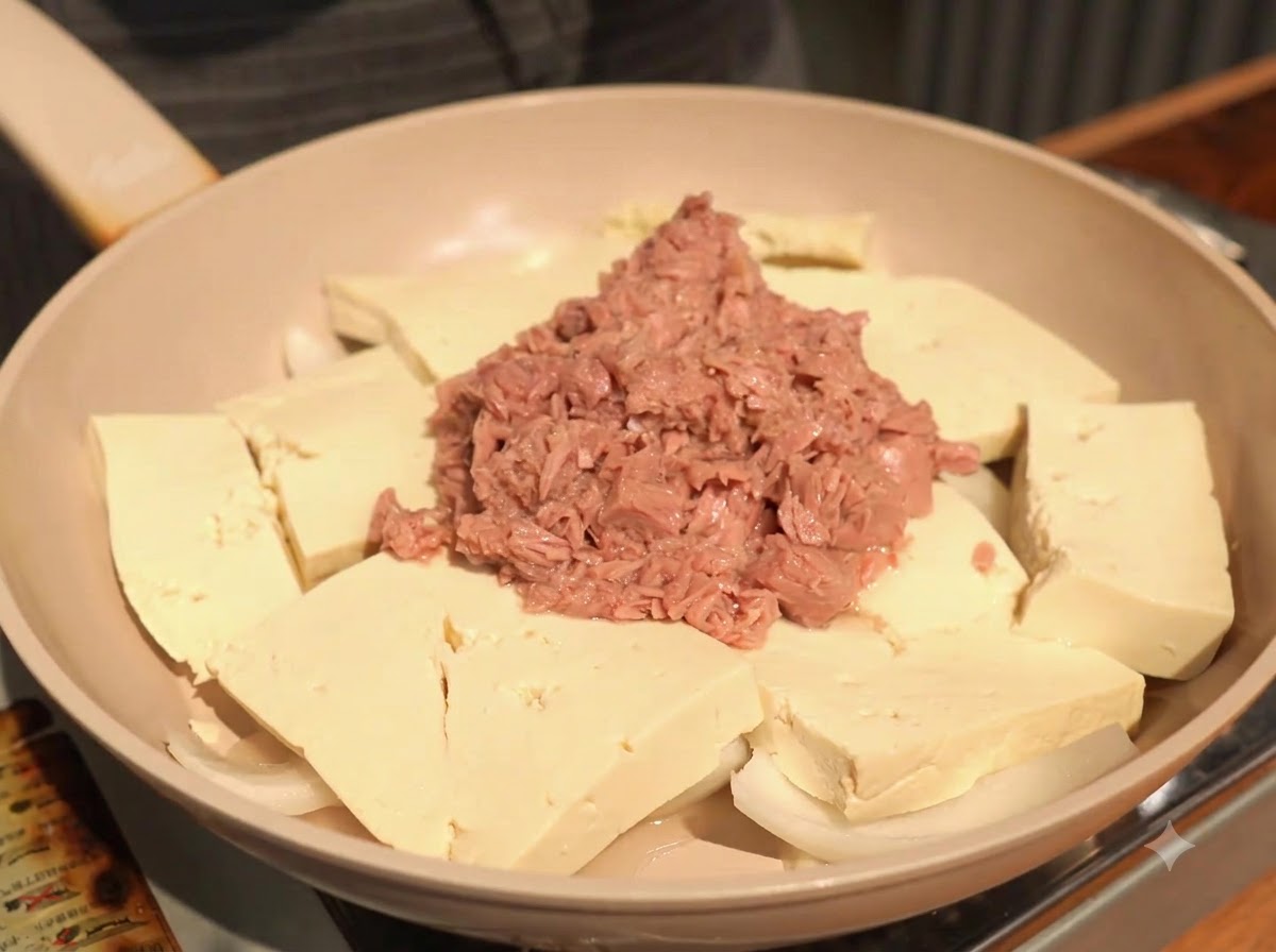 Dodawanie porcji posiekanego czosnku na patelnię, spoczywającego na tofu obok tuńczyka.