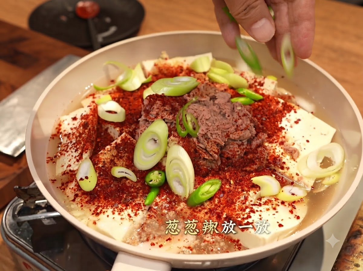 Dłonie rozsypujące pokrojoną zieloną cebulkę i zielone papryczki chili nad patelnią pokrytą płatkami chili, tofu i tuńczykiem.