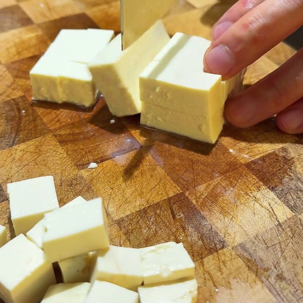 Jedwabiste tofu krojone w zgrabną, małą kostkę na drewnianej desce.