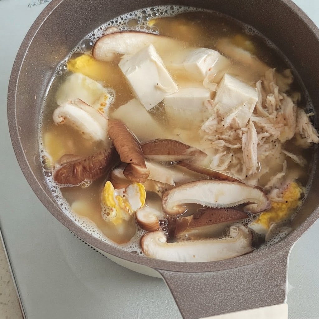 Mały kopczyk suszonych krewetek leżący na wierzchu gotującego się tofu, grzybów i jajka w garnku z bulionem.