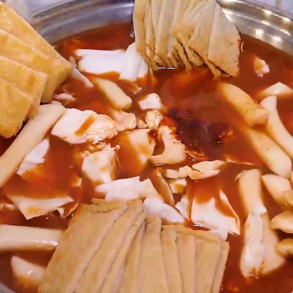 Zmontowany hot pot wypełniony kapustą, kluskami ryżowymi, ciastkami rybnymi, posypany smażonym tofu i zieloną cebulką.