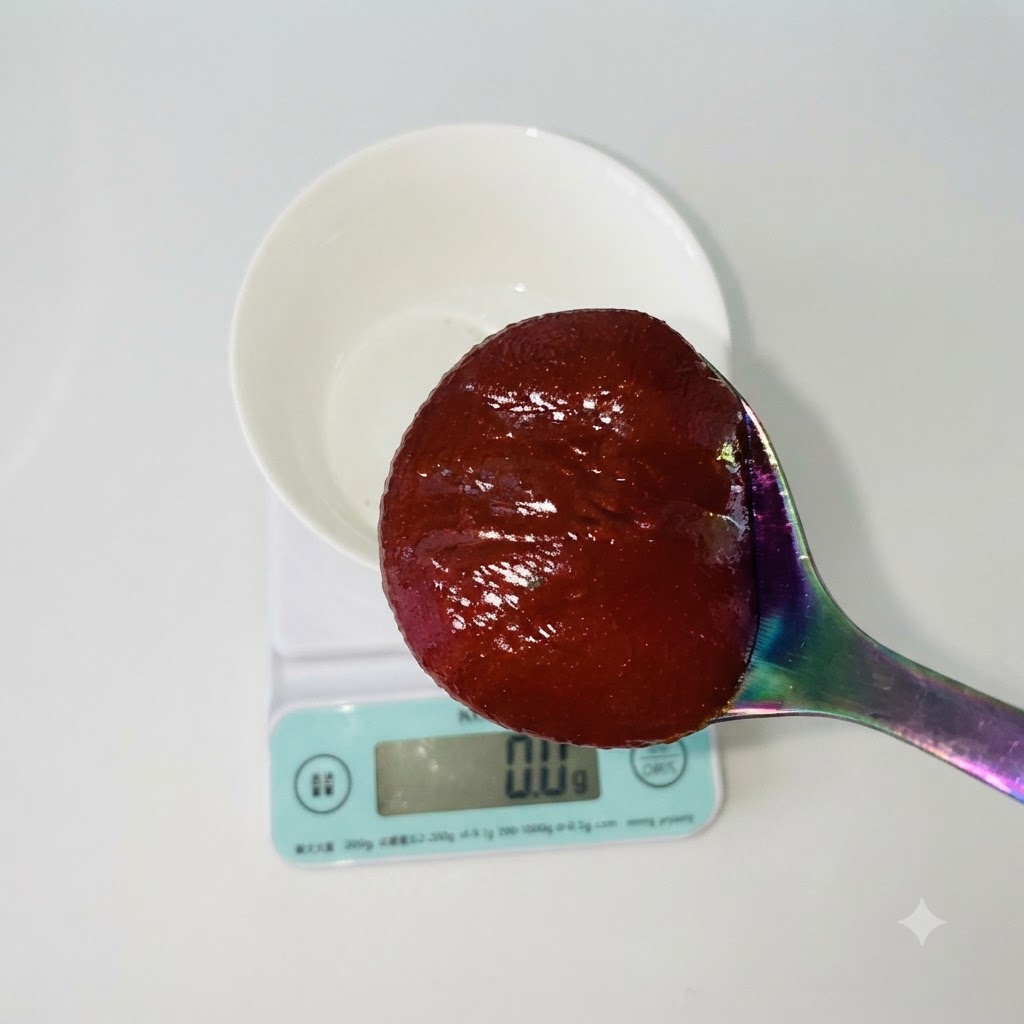 Łyżka czerwonej koreańskiej pasty chili trzymana nad białą miską stojącą na cyfrowej wadze kuchennej.