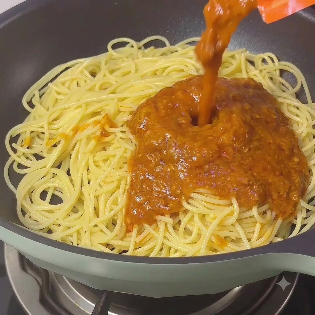 Bogaty, klasyczny sos boloński wlewany na nitki spaghetti na patelni.