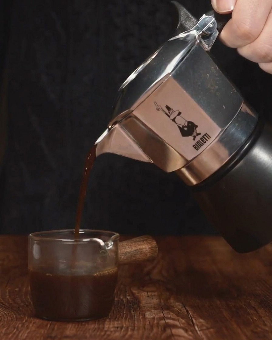 Ciemne espresso wlewane ze srebrnej kawiarki do małego szklanego pojemnika.