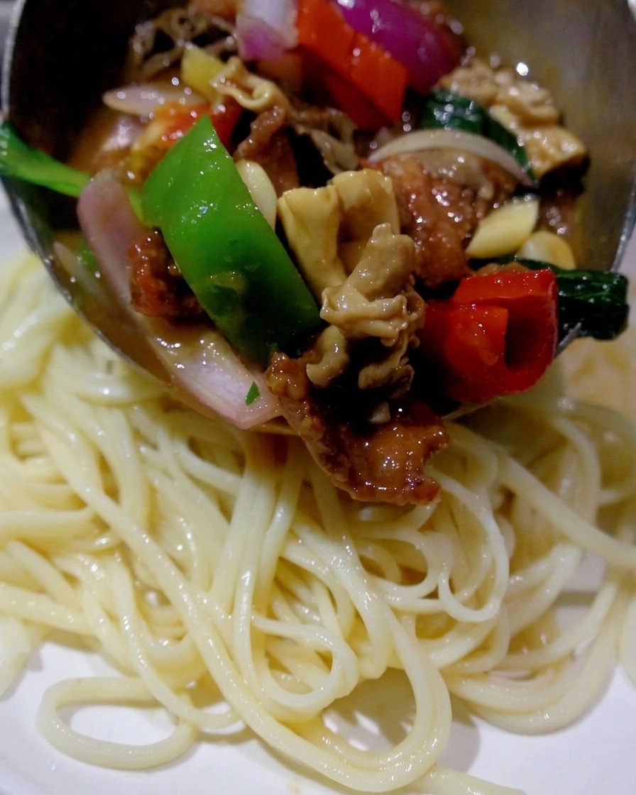 Łopatka nakładająca gorącą mieszankę stir-fry z grzybów, mięsa i papryki na talerz z ugotowanym makaronem.