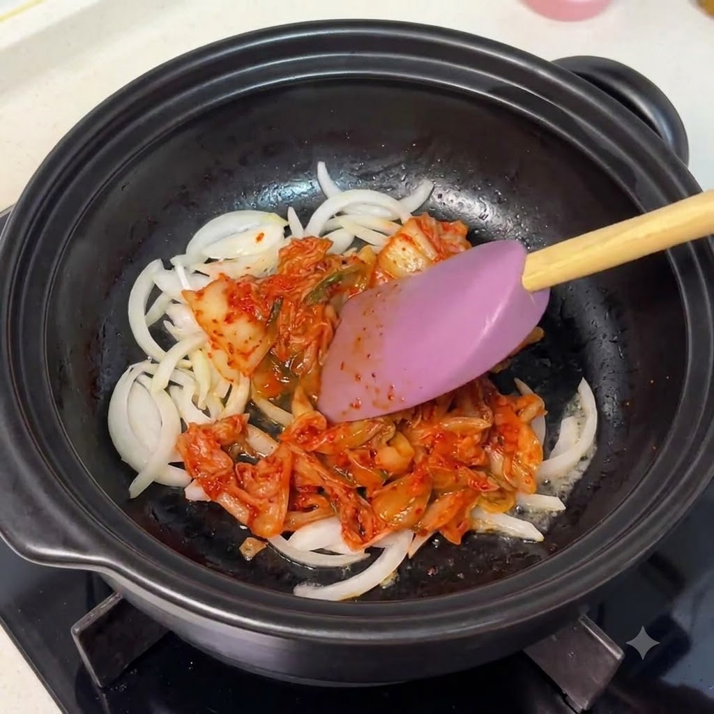 Posiekane kimchi mieszane z cebulą w czarnym garnku za pomocą łopatki.