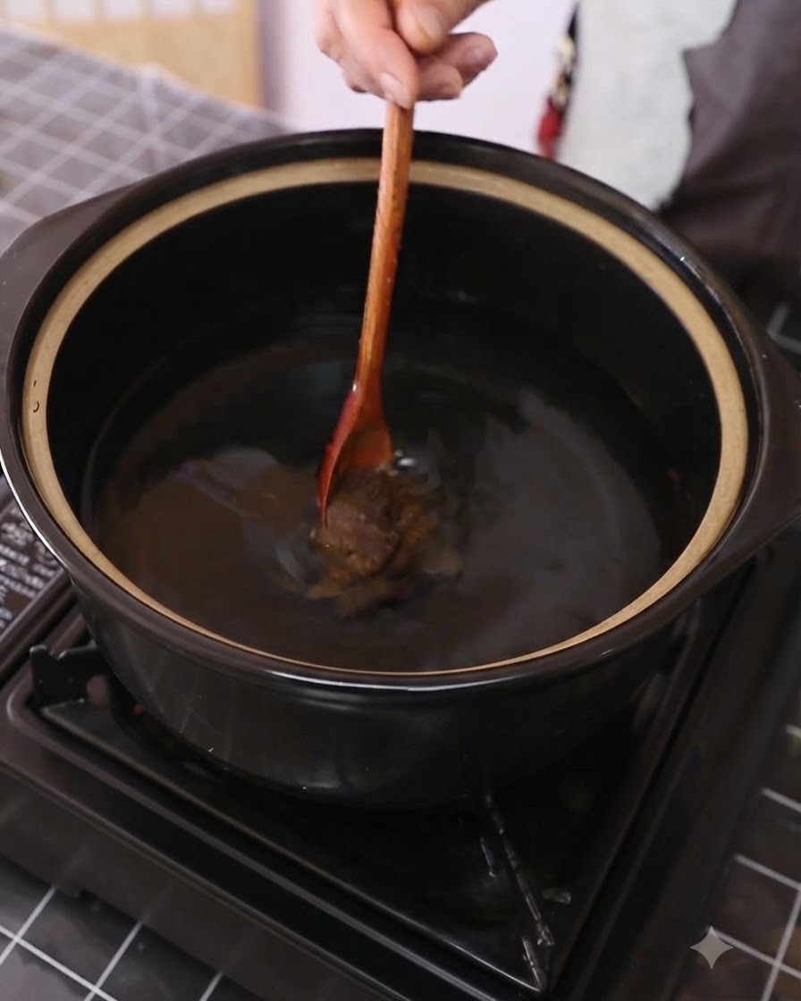 Pasta sojowa mieszana z wodą w ciemnym garnku za pomocą drewnianej łyżki.
