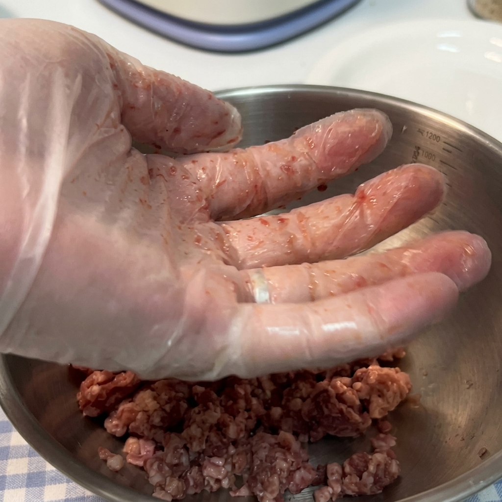 Ręka w rękawiczce podrzucająca surową kulkę wołową nad miską.