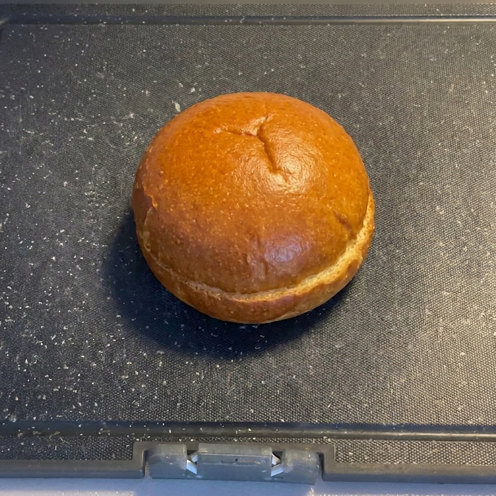 Połówki bułek do burgera leżące na ciemnej desce do krojenia.