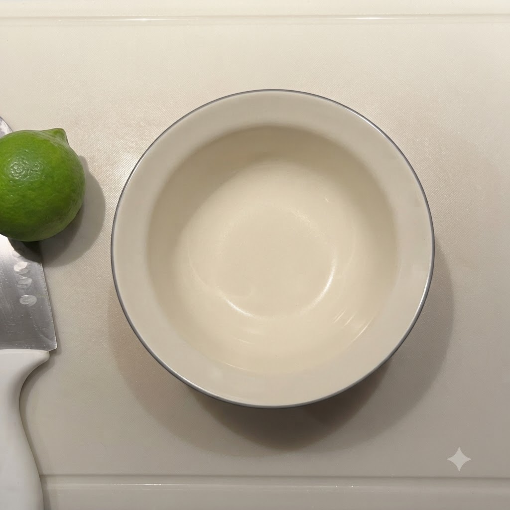 Pusta mała ceramiczna miseczka obok świeżej limonki i noża na desce do krojenia.