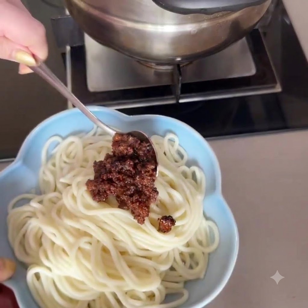 Zbliżenie przedstawiające łyżkę delikatnie nakładającą bogaty, brązowy sos mięsny na miseczkę białego makaronu.